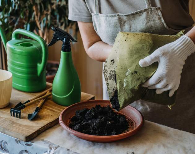 A person with white gloves pours the black mass into the tray of a flower pot