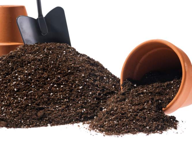 A black garden trowel in soil mix next to two terracotta pots.